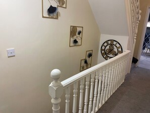 Eine Treppe mit weißer Brüstung, einer an der Wand montierten Uhr und dekorativen Wandbildern.