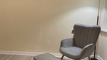 A room with a grey armchair and ottoman on a patterned rug, a floor lamp, and a wall art piece.