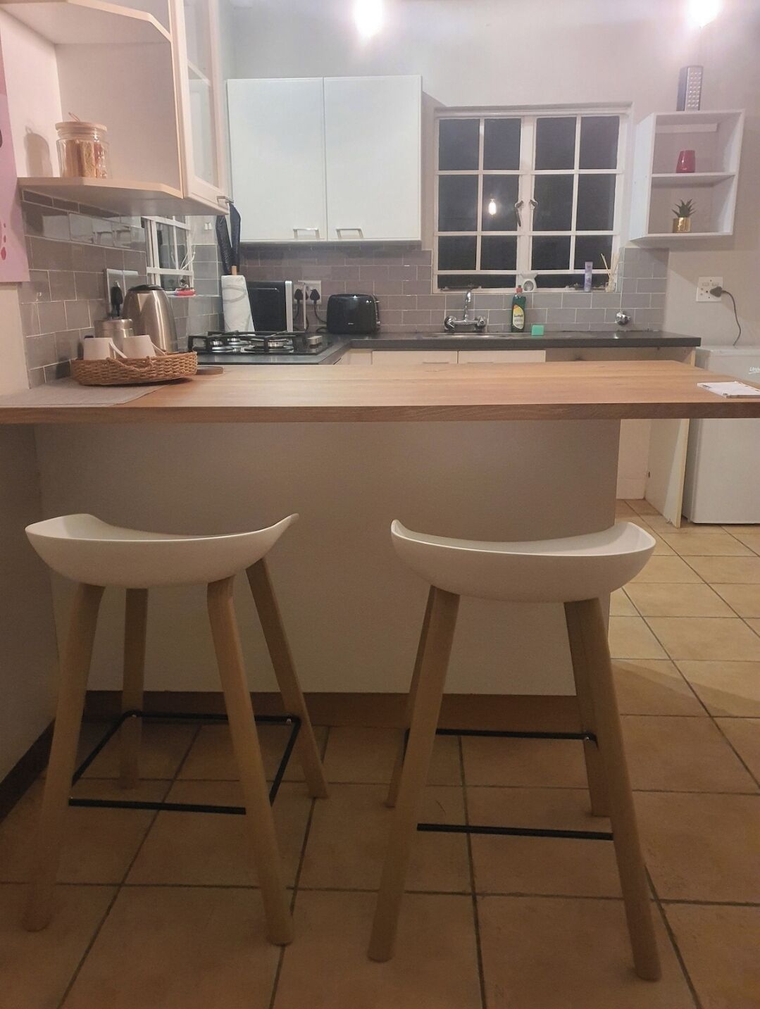 Una cucina con isola centrale, due sgabelli da bar, una finestra e un armadietto bianco.