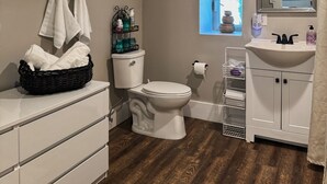 Ein Badezimmer mit Toilette und Waschbecken in Weiß, einem Spiegel und einem Fenster mit Außenblick.