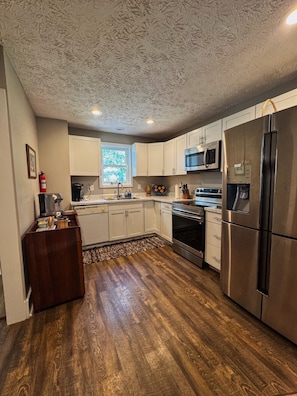 A kitchen with white cabinets, a stainless steel refrigerator, a microwave, and an oven.