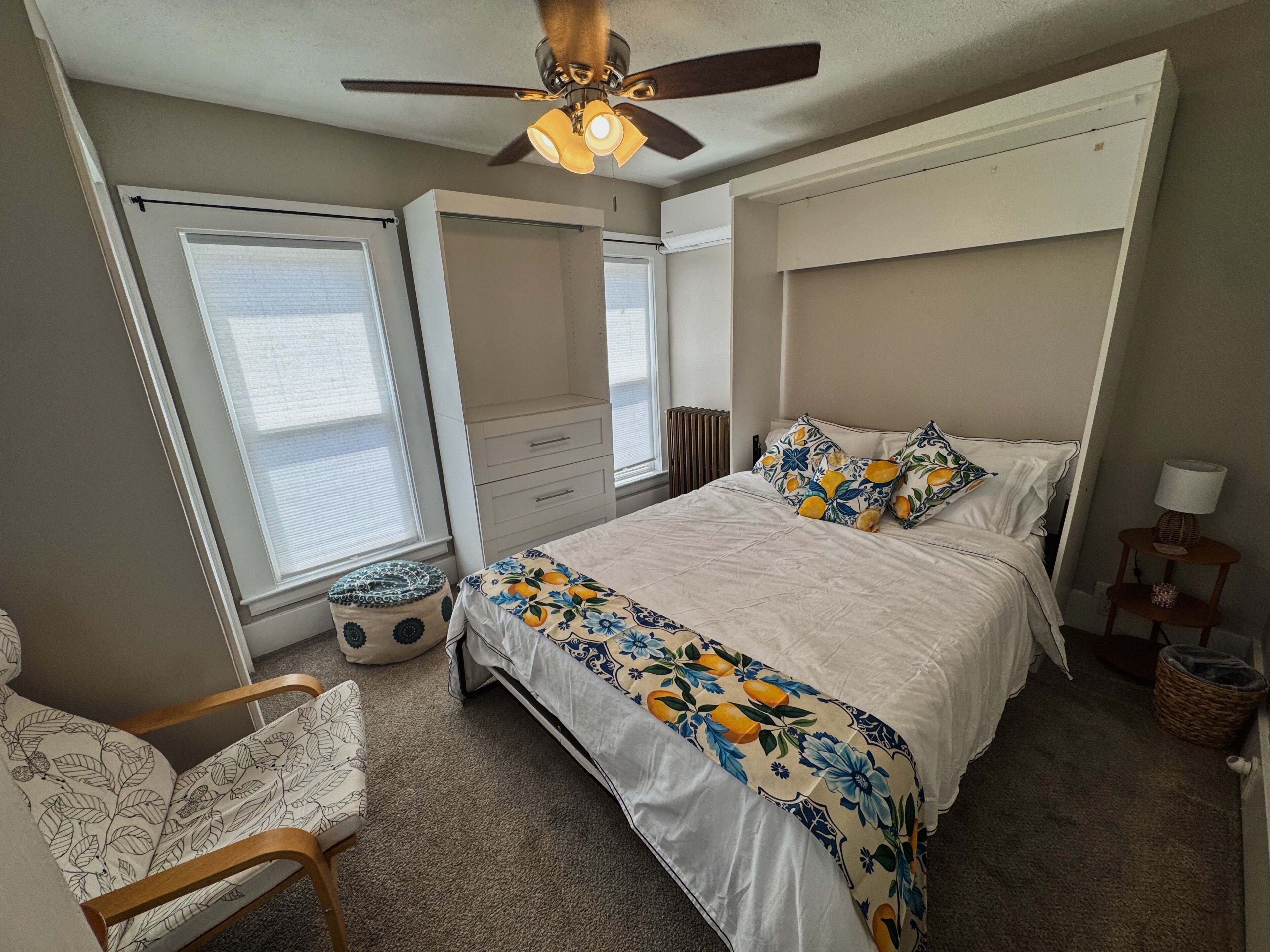 A bedroom with a bed, a chair, a ceiling fan, a window, and a radiator.
