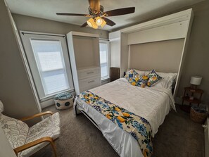 A bedroom with a bed, a chair, a ceiling fan, a window, and a radiator.