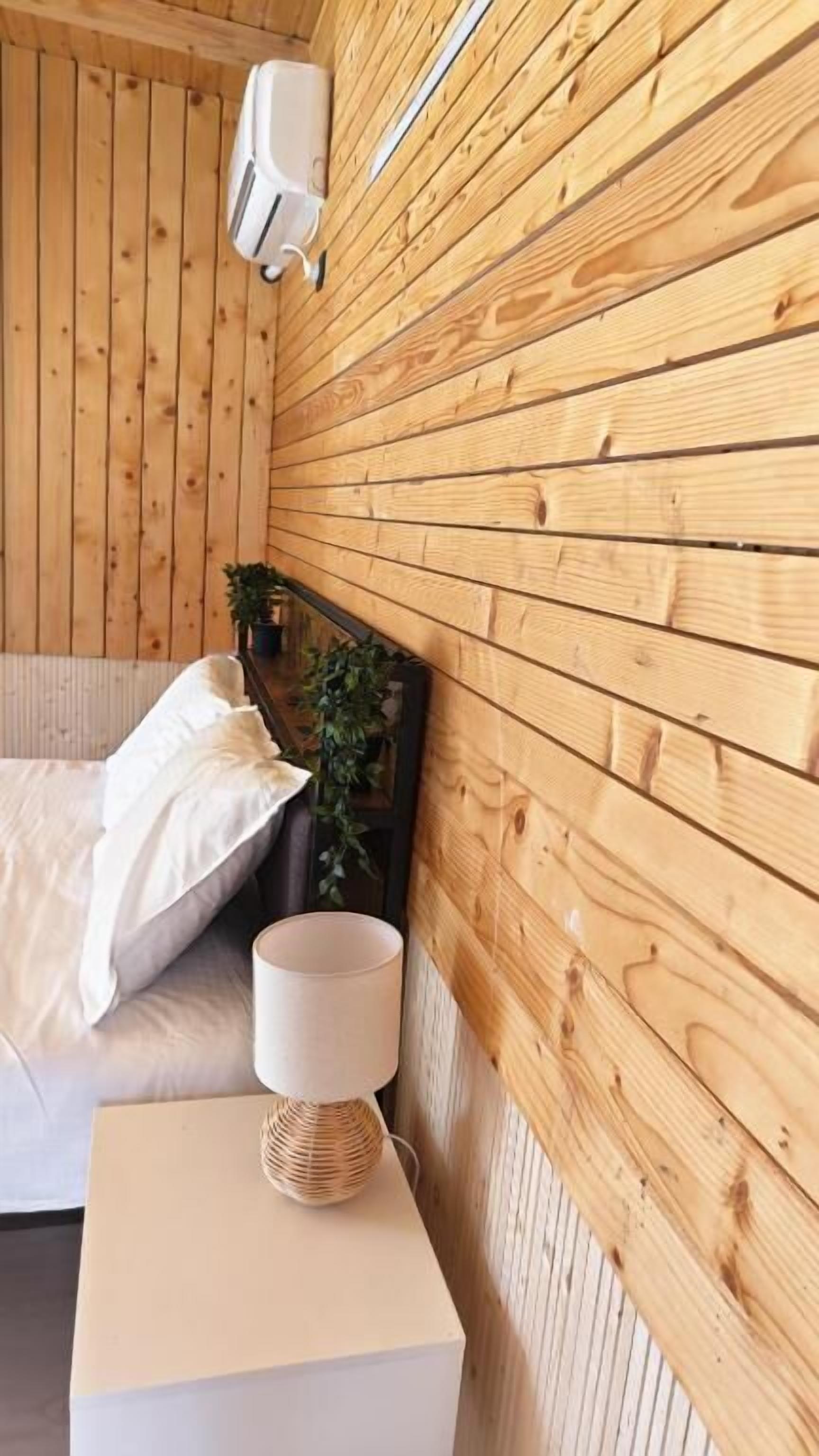 Una habitación con paneles de madera, una cama, una lámpara de noche y un calentador de pared.