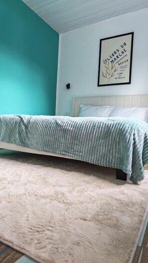 Un dormitorio con una cama, cabecera blanca, pared color esmeralda y un cuadro en la pared.