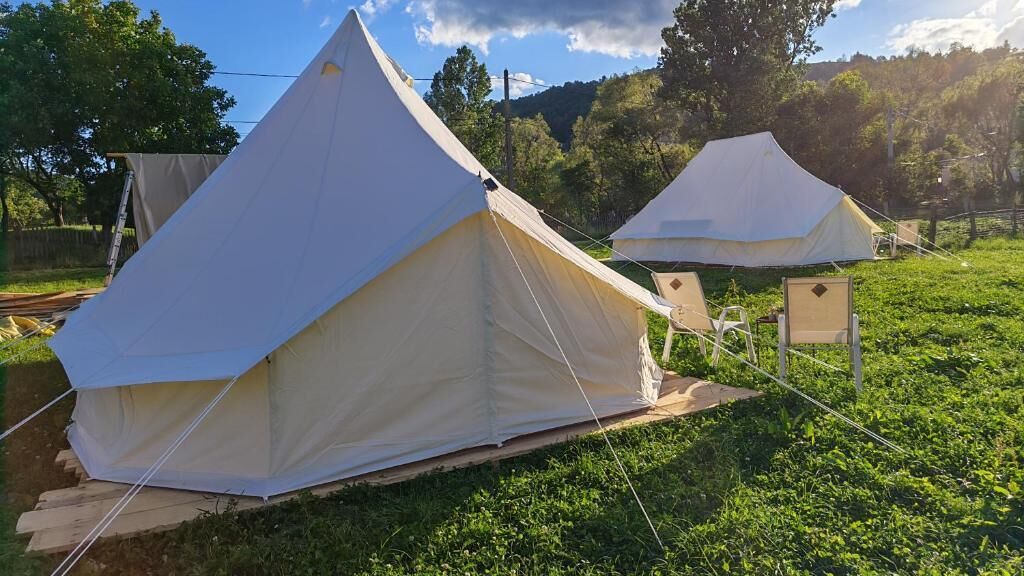 Two large, white tents set up on a grassy field with trees in the background.