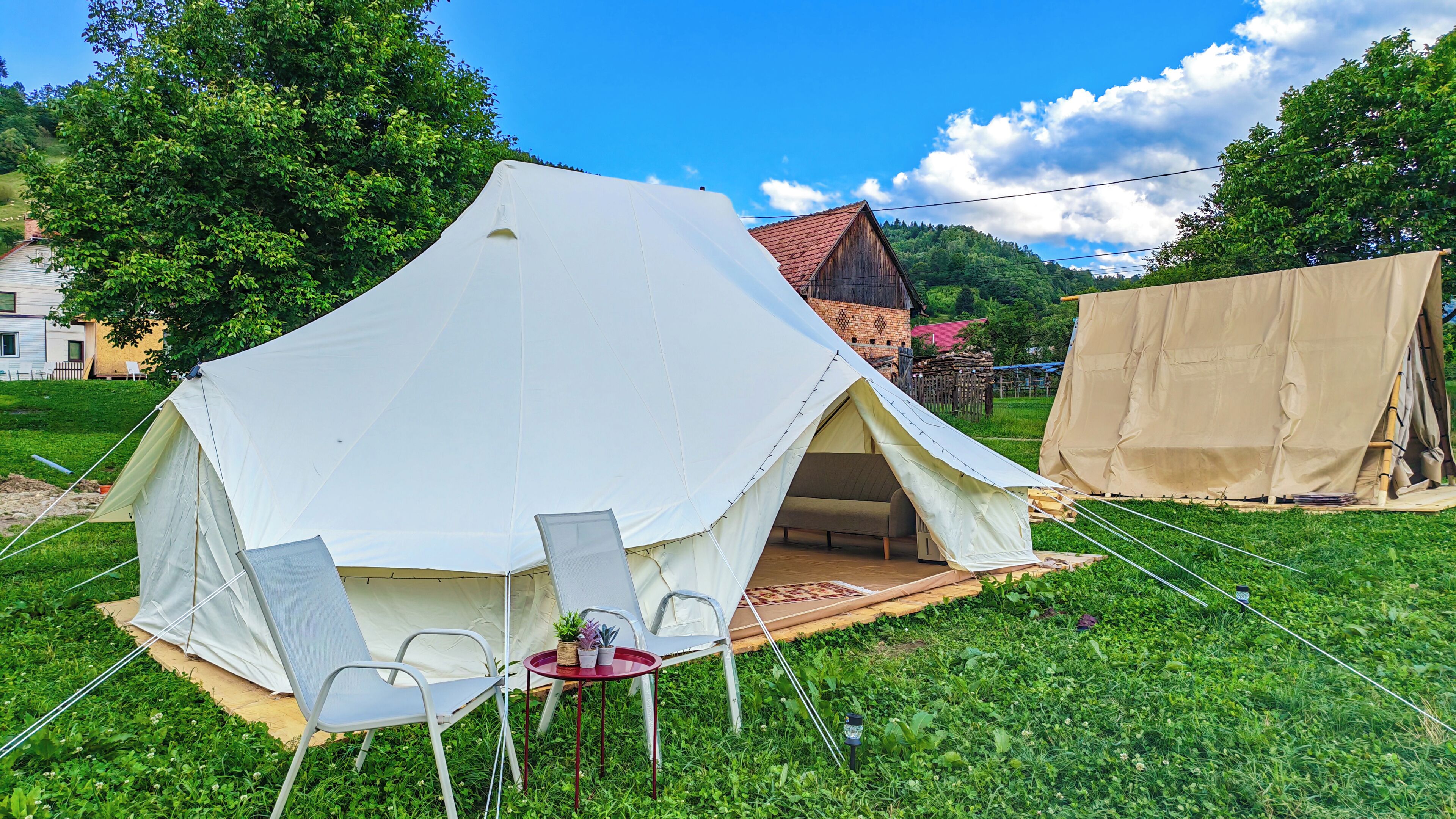 Una gran carpa blanca instalada en un área de césped, con una mesa y sillas cerca.