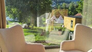 Una habitación con dos sillas frente a un amplio ventanal con vistas a un jardín y un edificio.