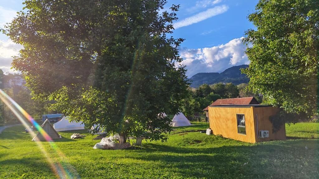 Un campamento con tiendas de campaña y un pequeño edificio de madera, rodeado de árboles y césped.