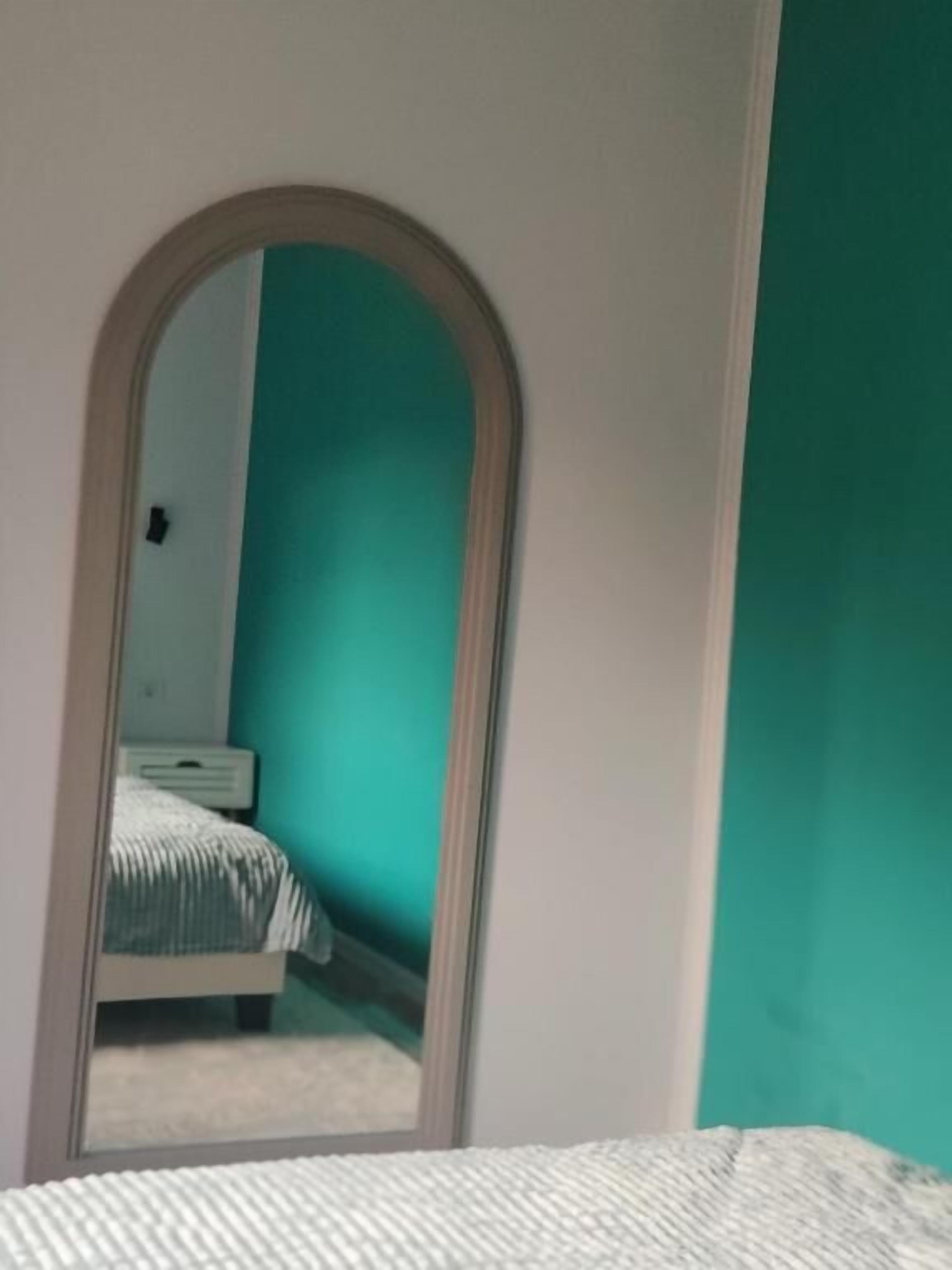 A room with a bed, a mirror, and a teal-colored wall.