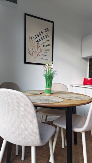 A dining area with a round table, six chairs, a framed sign on the wall, and a vase with flowers.