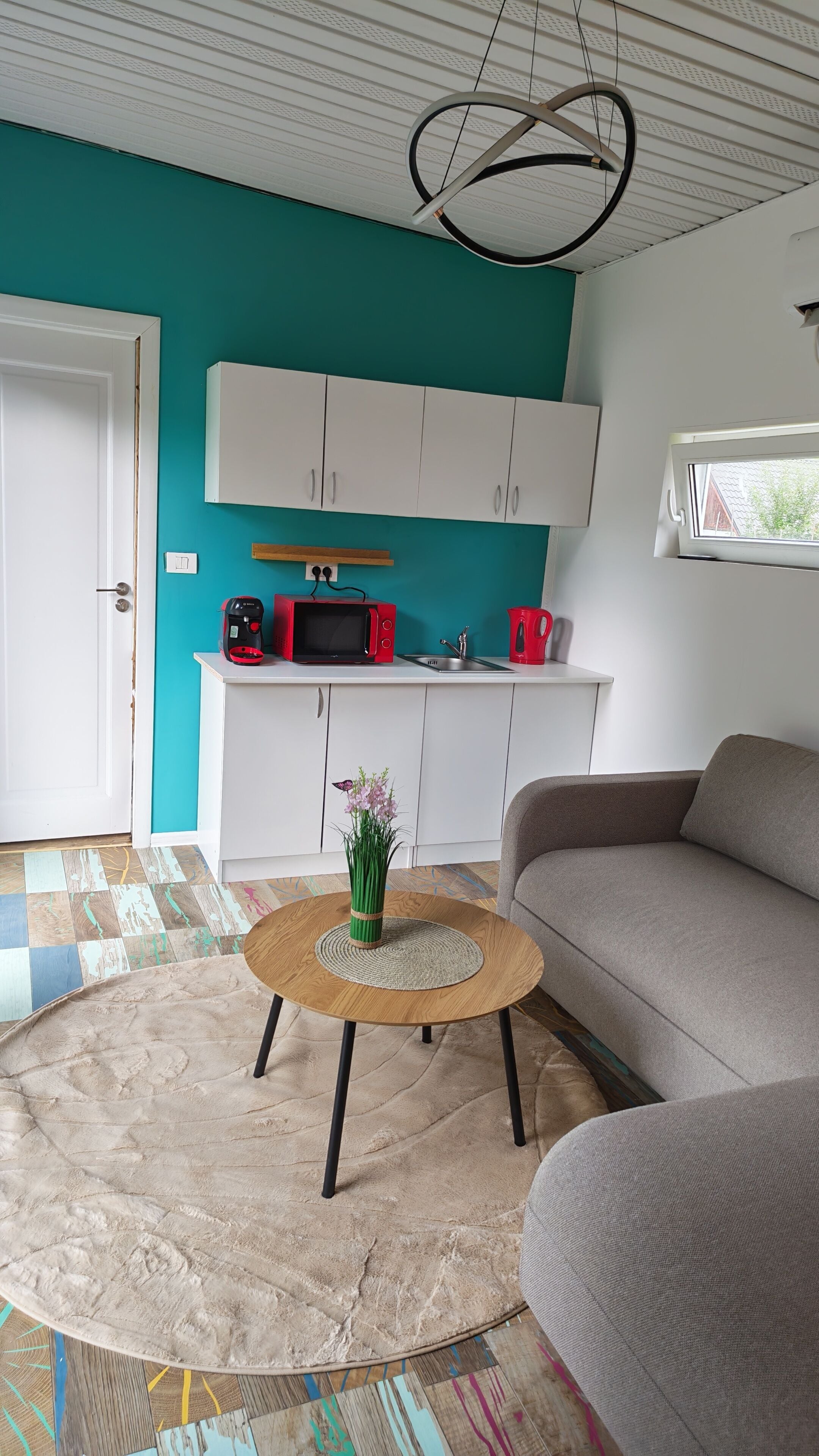 Un salón moderno con una pared verde azulado, armarios blancos, una mesa redonda de centro y un sofá gris.