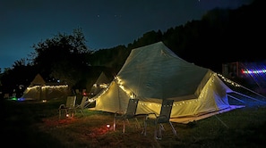A row of tents with string lights, arranged in a campsite with chairs in front.