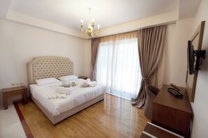 A hotel room with a large bed, a wooden floor, a chandelier, a desk, and a TV mounted on the wall. - CORALI RESORT (Agrinio)