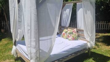 A four-poster bed with white canopies, set on a wooden frame, surrounded by grass and trees.