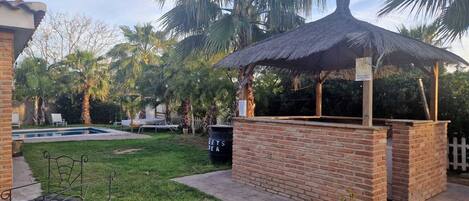 A backyard with a swimming pool, a brick gazebo, and palm trees.