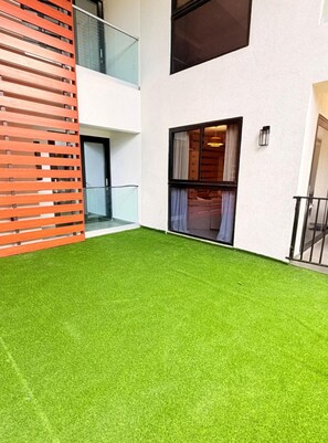 A modern building with a flat roof, a balcony with glass railings, and a green artificial lawn. - 2BR Comfy City Apartment - The Rogers (Kingston)