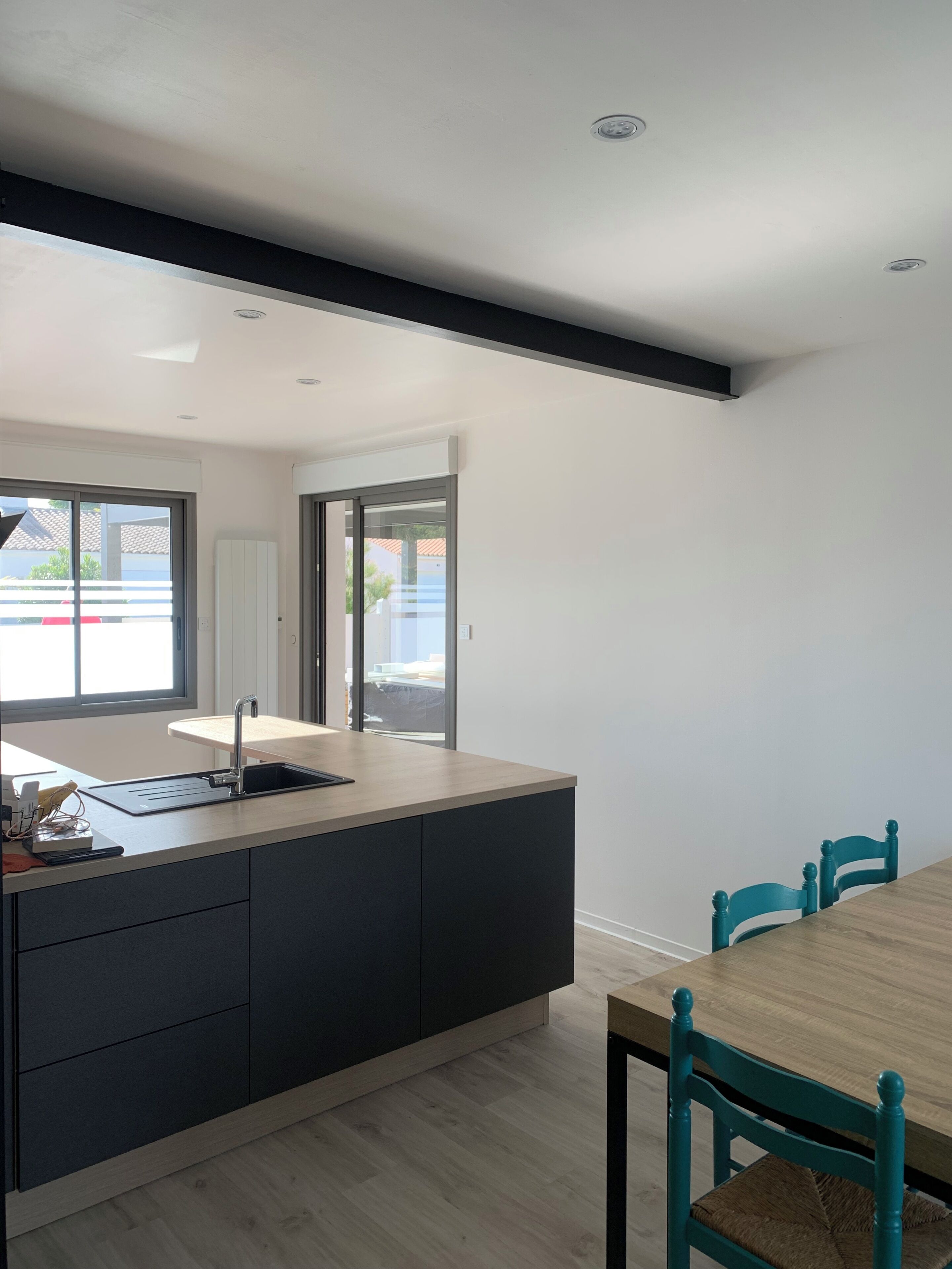Une cuisine moderne dotée d’un îlot central intégré, un coin repas avec une table et des chaises en bois, et une vue dégagée grâce à une porte ouverte.