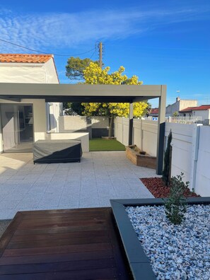 A modern outdoor patio with a wooden deck, a covered seating area, and a small garden with pebbles and plants. - Fenced detached house 600m from the sea (La tranche sur mer)
