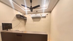 Zona de recepción con mostrador, ventilador de techo, unidades de aire acondicionado y televisión montada.