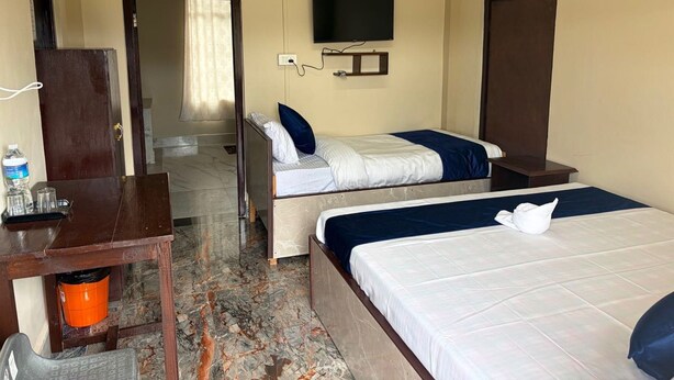 Habitación de hotel con dos camas, un televisor, un escritorio con silla, y un baño visible a través de una puerta abierta.