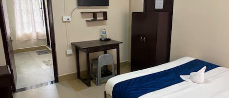 A hotel room with a bed, a desk, a television, a wardrobe, and a door leading to another room.