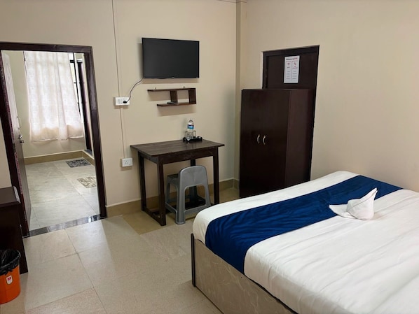 A hotel room with a bed, a desk, a television, a wardrobe, and a door leading to another room.