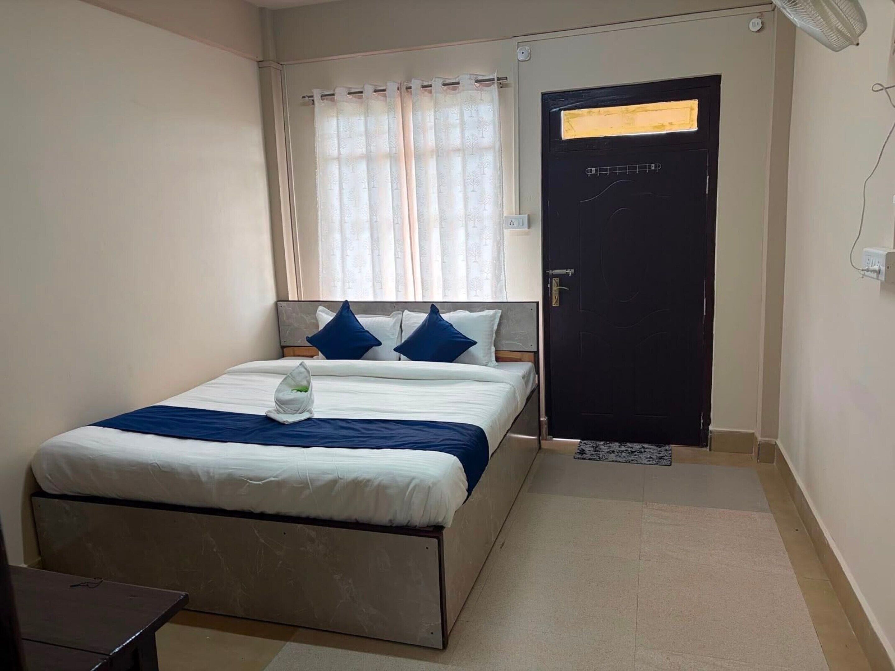 A bedroom with a bed, a window with curtains, a door, and a small table.