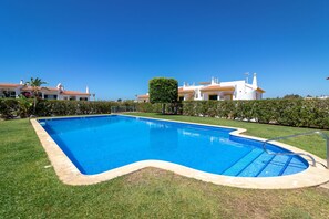 A swimming pool with a clear blue water, surrounded by well-maintained grass and a hedge. - Casa Vista Mar - 2 Bed Apt With Sea Views & Communal Pool (Carvoeiro)