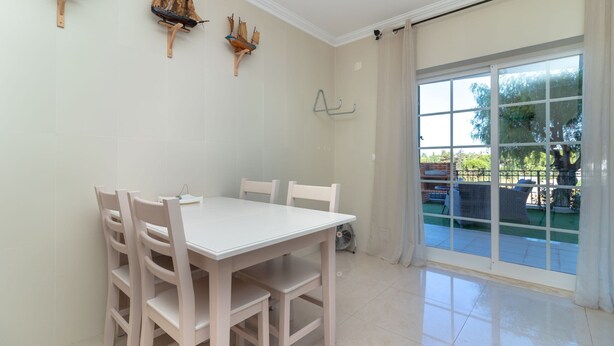 A dining area with a white table and chairs, a window with a view of the outdoors, and decorative ship models on the wall. - Casa Vista Mar - 2 Bed Apt With Sea Views & Communal Pool (Carvoeiro)