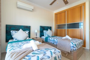 A hotel room with two beds, a ceiling fan, an air conditioning unit, and a wooden wardrobe. - Casa Vista Mar - 2 Bed Apt With Sea Views & Communal Pool (Carvoeiro)