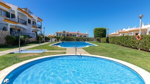 A swimming pool with a clear blue water surface, surrounded by a well-maintained lawn and a building with balconies. - Casa Vista Mar - 2 Bed Apt With Sea Views & Communal Pool (Carvoeiro)