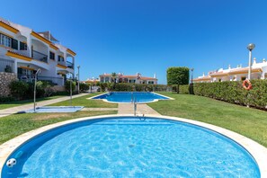 A swimming pool with a clear blue water surface, surrounded by a well-maintained lawn and a building with balconies. - Casa Vista Mar - 2 Bed Apt With Sea Views & Communal Pool (Carvoeiro)