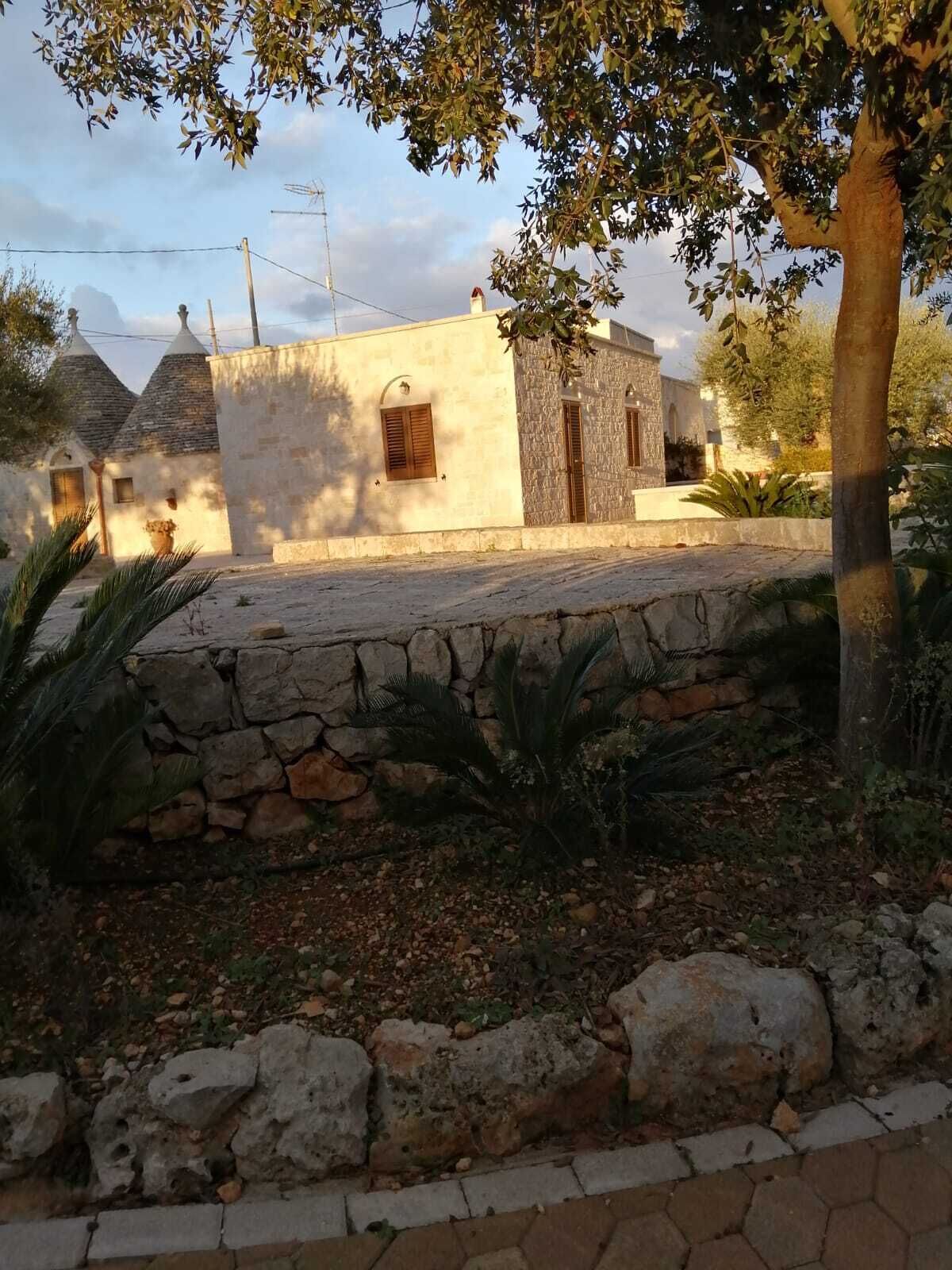 Un muro de piedra con un camino empedrado que conduce a un edificio de fachada pétrea y una ventana pequeña.
