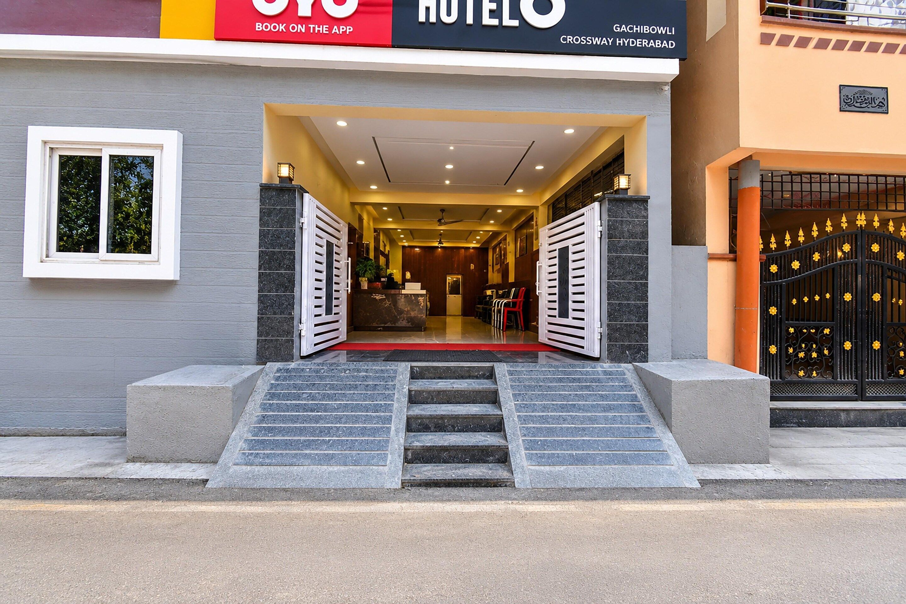 A hotel entrance with a red carpet, a staircase leading up, and a black gate with yellow flowers.