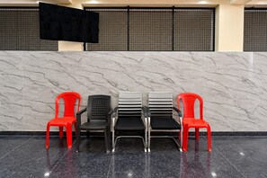 A reception area with a marble wall, a black screen, and four chairs in red and black. - Hotel Gachibowli Formerly Astra (Hyderabad)