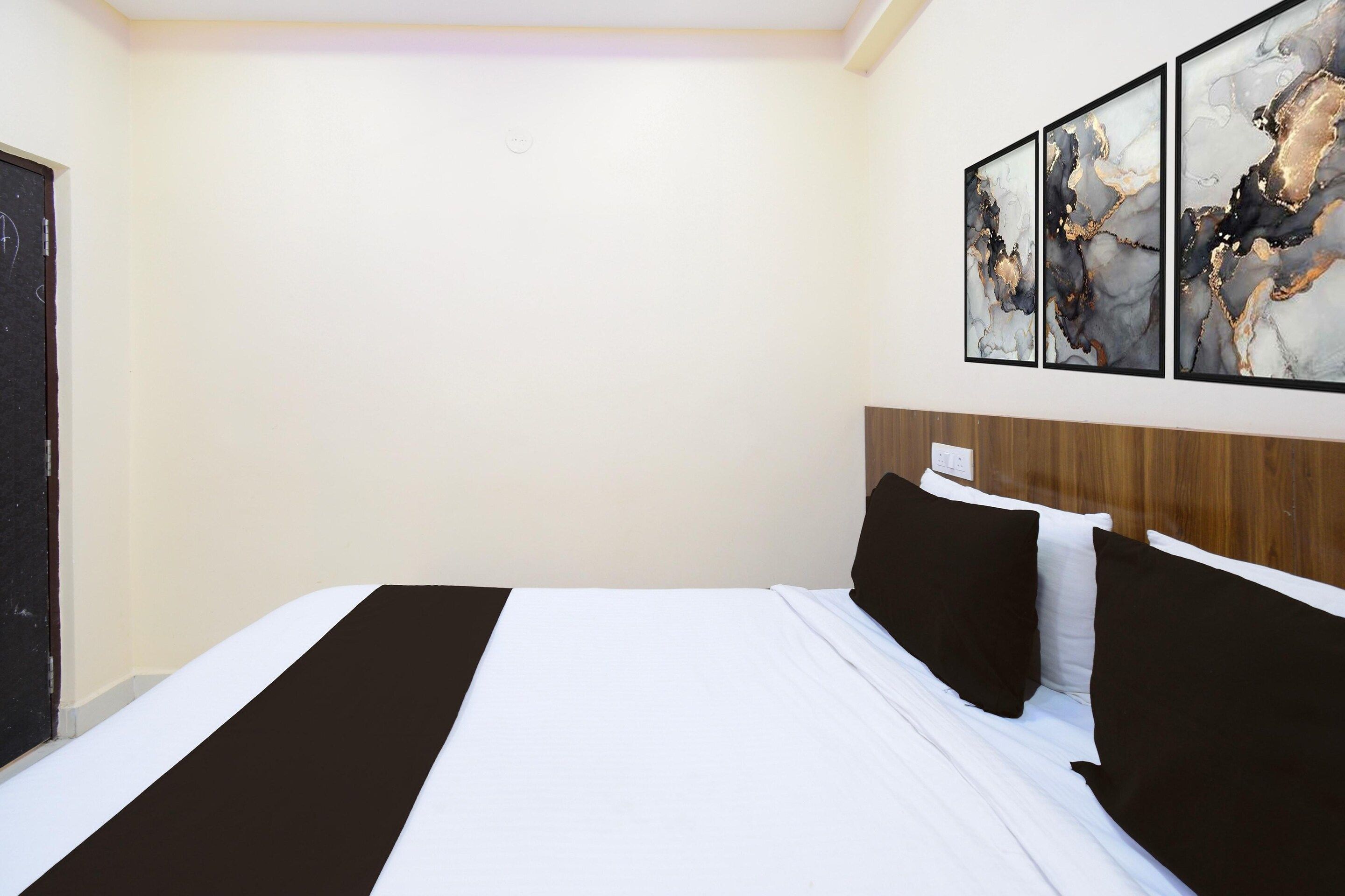 A hotel room with a bed, a wooden headboard, and three abstract paintings on the wall.