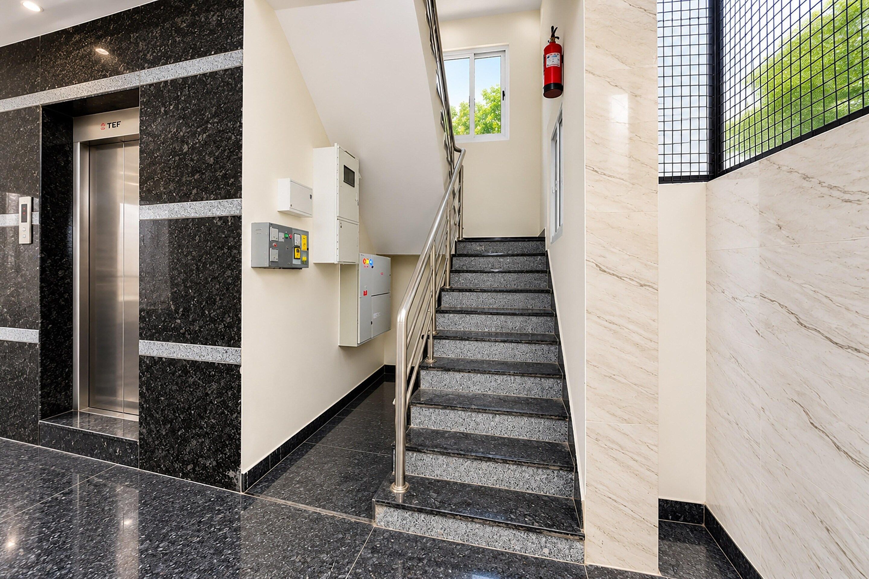 A modern interior with a marble staircase, an elevator, and a fire extinguisher.