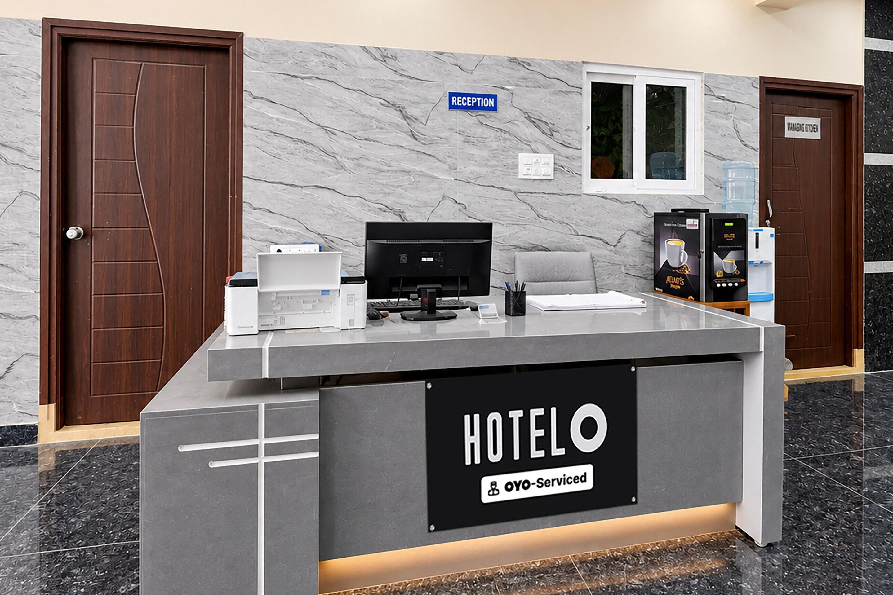 Una reception d'hotel con una parete in marmo, insegna della reception e una macchina per il caffè.