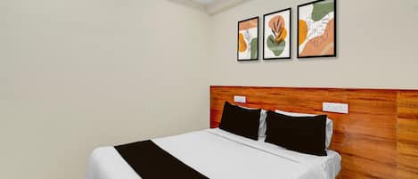 Une chambre d’hôtel avec un lit, une tête de lit en bois et trois œuvres d’art encadrées accrochées au mur.