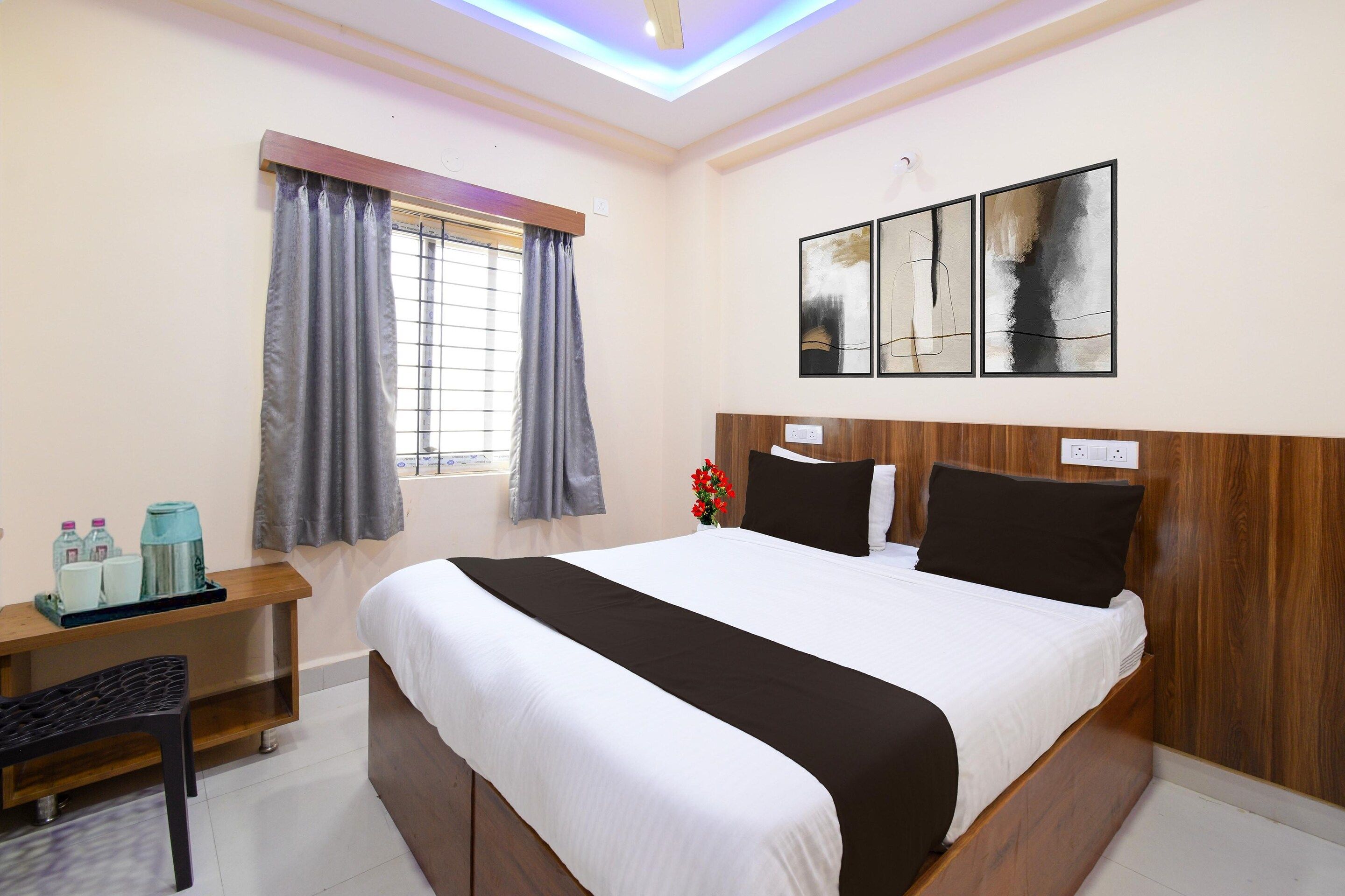 Une chambre d’hôtel avec un lit, un bureau et une chaise, une fenêtre avec des rideaux et des œuvres d’art accrochées au mur.