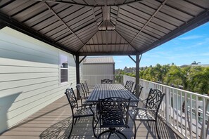 Eine überdachte Terrasse im Freien mit Tisch und Stühlen, mit Blick auf ein Gewässer und Palmen.