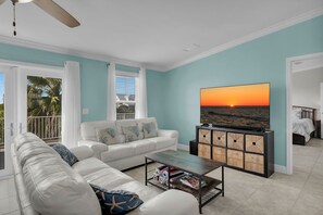 A living room with a white sofa, a coffee table, and a TV displaying a sunset. - Walk to Sombrero Beach - 85' Dock, Views (Marathon)