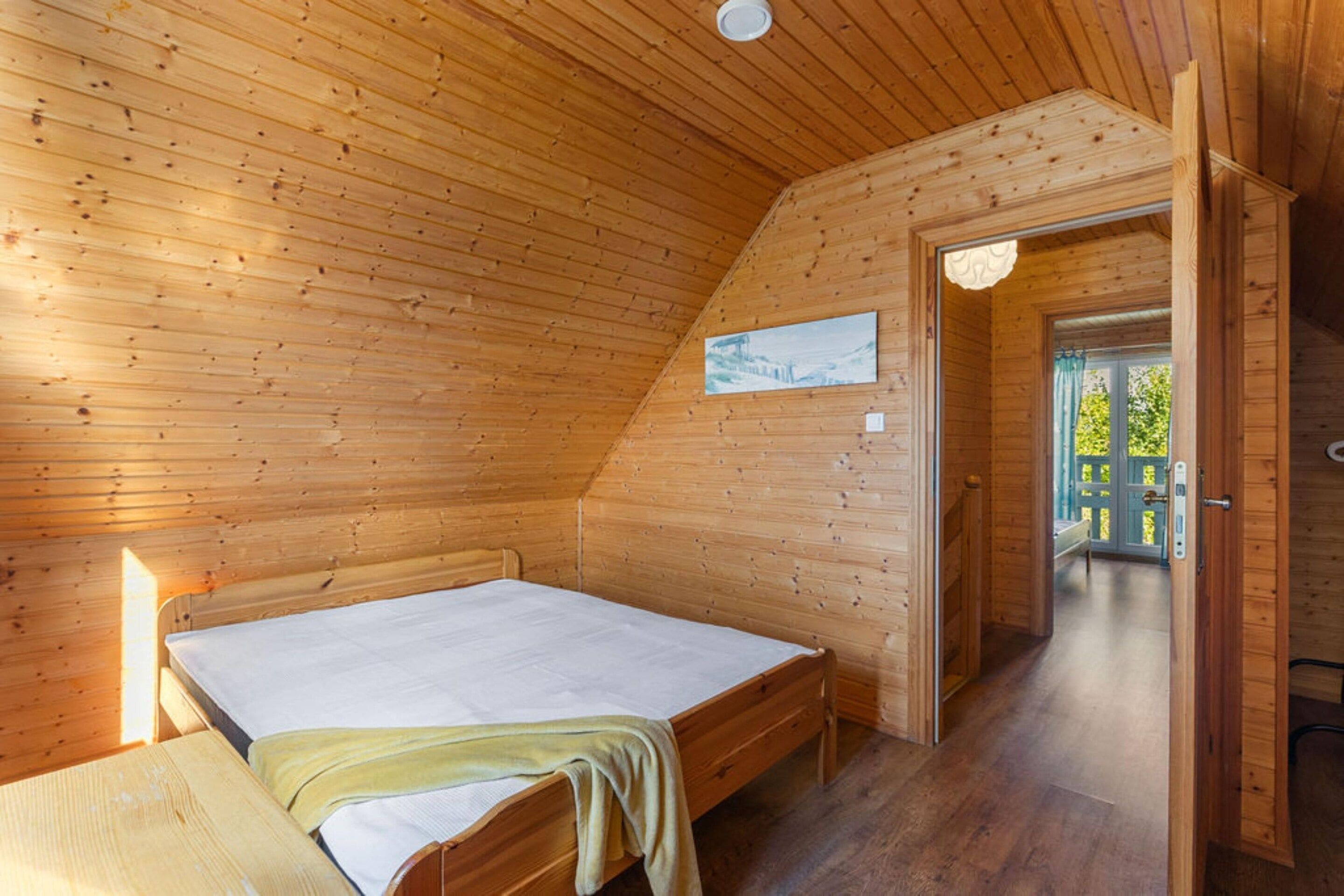 A wooden-paneled room with a bed, a door leading outside, and a small painting on the wall.