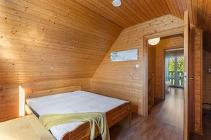 A wooden-paneled room with a bed, a door leading outside, and a small painting on the wall. - Comfortable Holiday Home With a Fireplace (Darlowo)
