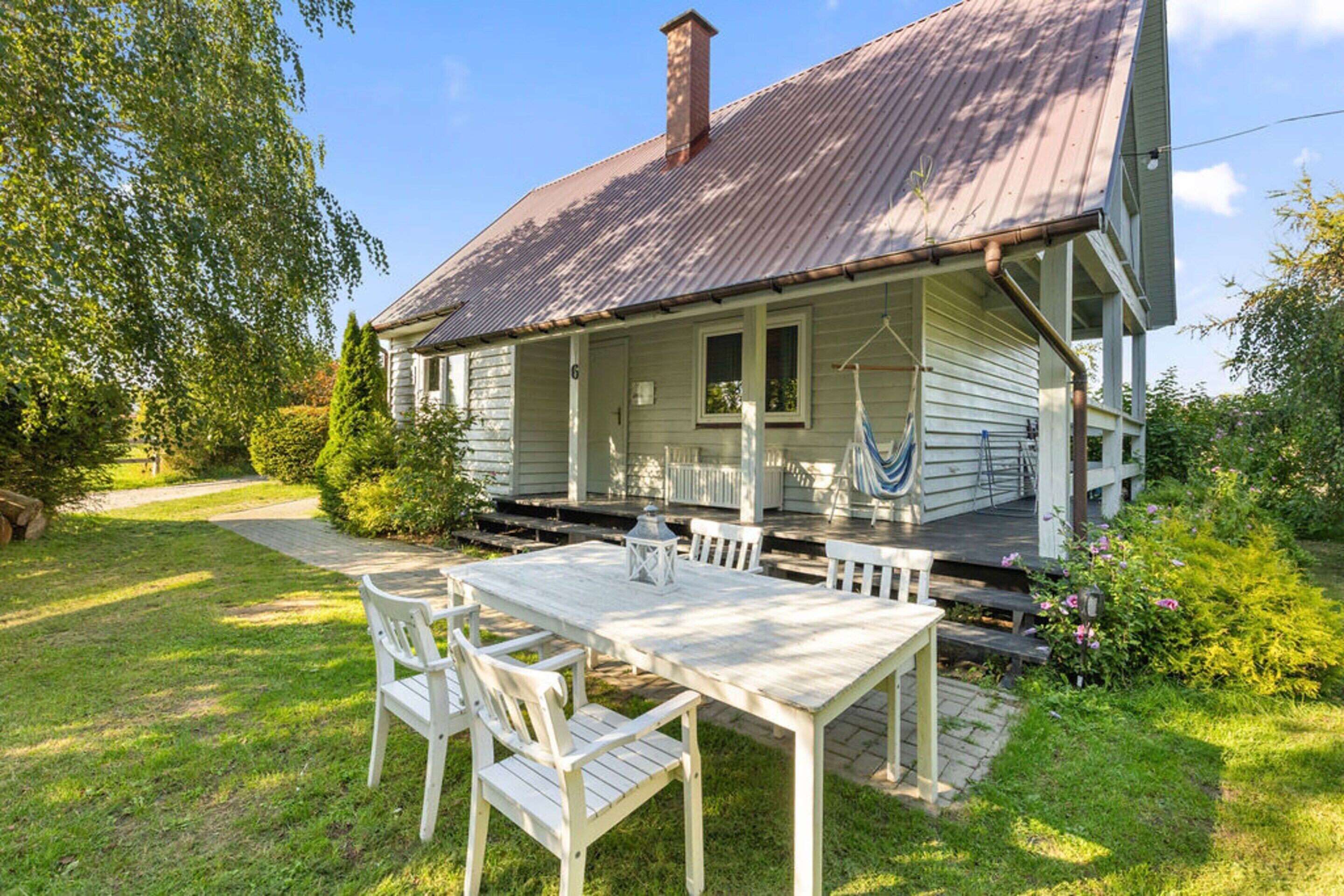 A two-story house with a porch, a dining table with chairs, and a hammock.