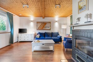 A living room with a wooden ceiling, a fireplace, a blue sofa, a white coffee table, and a television on a white cabinet. - Comfortable Holiday Home With a Fireplace (Darlowo)
