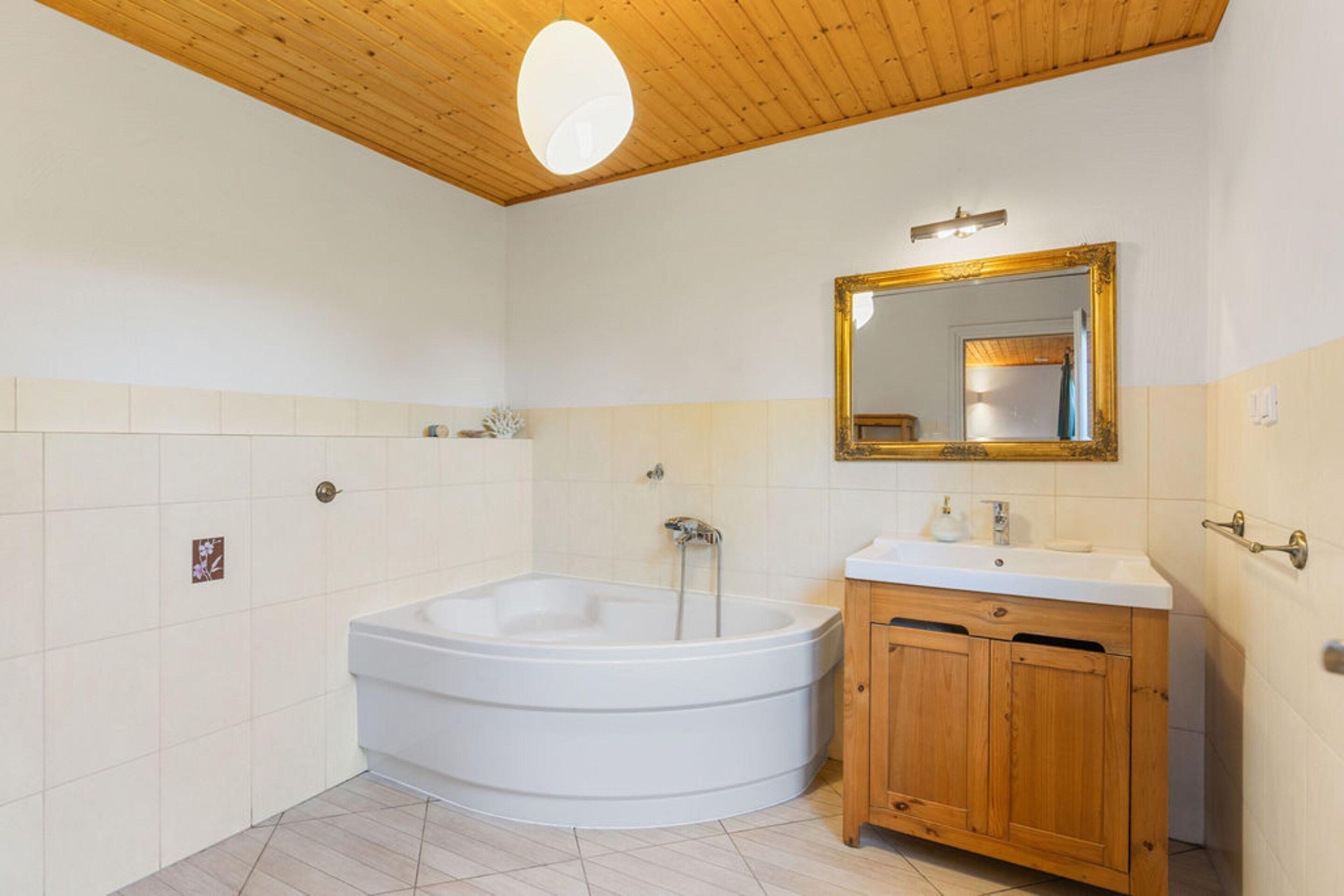A bathroom with a freestanding bathtub, a wooden vanity, and a mirror with a gold frame.
