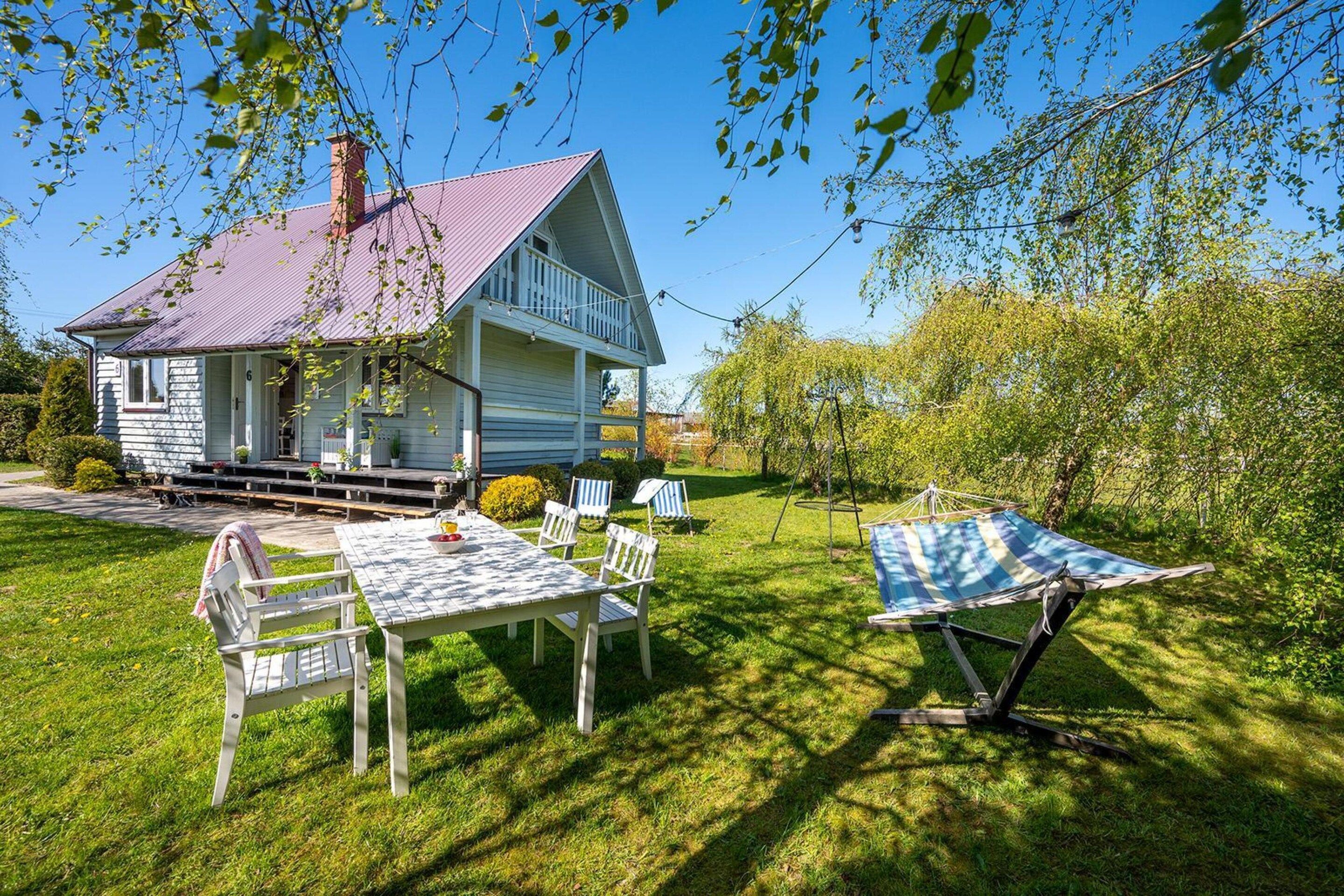 A house with a porch, a dining table with chairs, and a hammock in the yard.