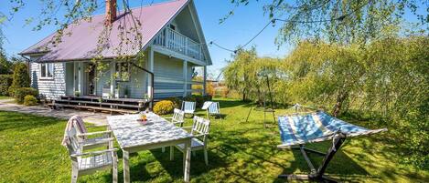 Une maison avec une véranda, une table à manger avec des chaises et un hamac dans le jardin.